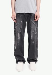 Μαύρο τζιν παντελόνι με μεγάλες λευκές κεντητές σχεδόν αστραπές στο μπροστινό μέρος. Χαλαρή εφαρμογή με πέντε τσέπες και λεπτομέρειες με φθαρμένο τελείωμα.