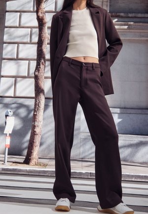 Bruine op maat gemaakte broek gecombineerd met een crèmekleurig geribbeld crop top en een bijpassende blazer, met een ontspannen pasvorm en strakke lijnen.