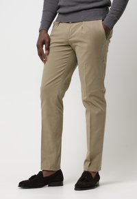 Beige Baumwollhosen im Slim-Fit, ausgestattet mit Vorderaschen und einer glatten Oberfläche, kombiniert mit dunklen Wildleder-Slippern.
