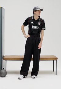 Juoda sportinė liemenė su baltais ir raudonais akcentais, derinama su juodomis, aukštu liemeniu kelnėmis. Pilka kepurė ir balti sportbačiai užbaigia įvaizdį.