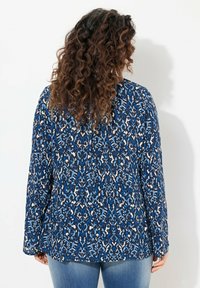 Blusa blu a fantasia con maniche lunghe, caratterizzata da un motivo floreale in varie tonalità di blu e crema, realizzata in un tessuto leggero.