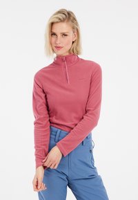 Pullover in pile di un delicato rosa con colletto alto e chiusura a mezza zip. Maniche lunghe, tessuto testurizzato, abbinato a pantaloni azzurri chiari.