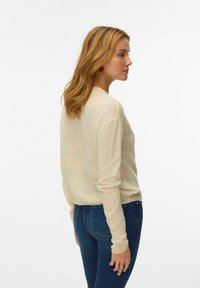 Pull beige clair à coupe décontractée, col rond et manches longues, associé à un jean bleu foncé. Tissu en tricot texturé.