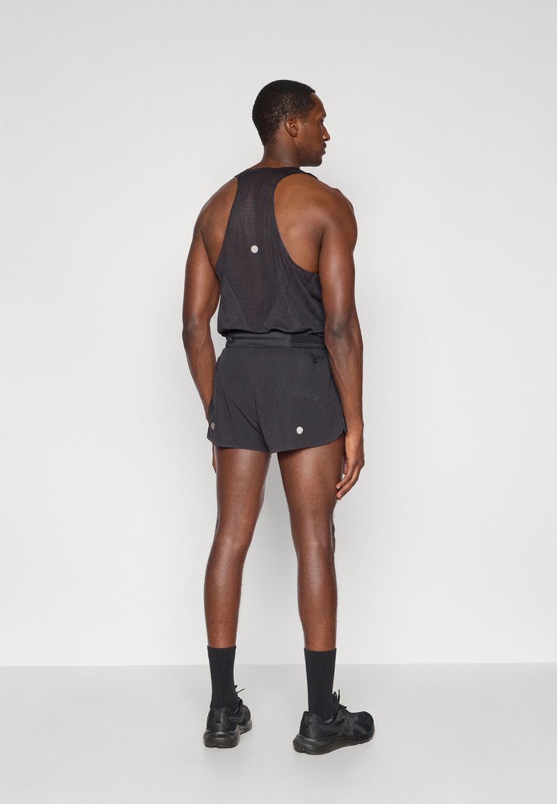 Débardeur de sport noir avec un design dos nageur, associé à un short noir. Il présente des accents réfléchissants et un tissu texturé pour la respirabilité.