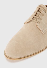 Beige suede oxford shoe with a pointed toe, six eyelets for laces, and a thin brown leather sole. Smooth texture with minimal stitching.