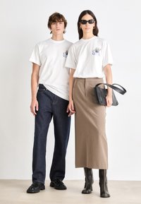 Kortærmede hvide t-shirts med blomsterbroderi, parret med mørke denimbukser og en brun midikjole. Sorte knæhøje støvler og en sort taske.