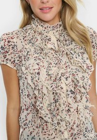 Lightweight, cream blouse with a ruffled design, featuring small floral patterns in red and navy, and a high, pleated collar.
