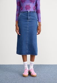 Jupe en denim de coupe droite, longueur mi-mollet, avec une couture frontale. Associée à des baskets roses et des chaussettes rayées blanches.