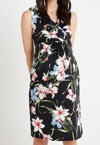 Vestido negro floral con diseño sin mangas, que presenta patrones de flores en blanco, rosa y azul, con cintura fruncida y material ligero.