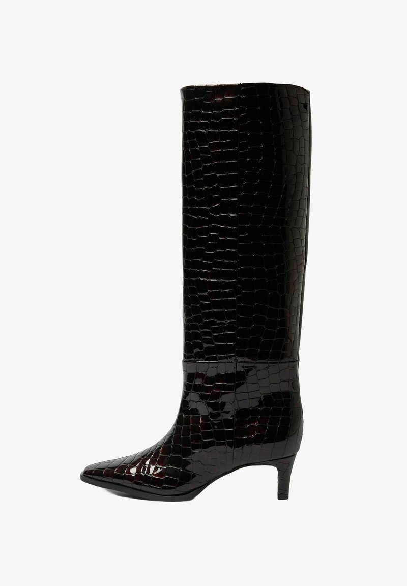 Musta põlveni ulatuvad saapad läikiva krokodillinahka meenutava mustriga. Disaini lõpetavad terav nina ja peen konts.