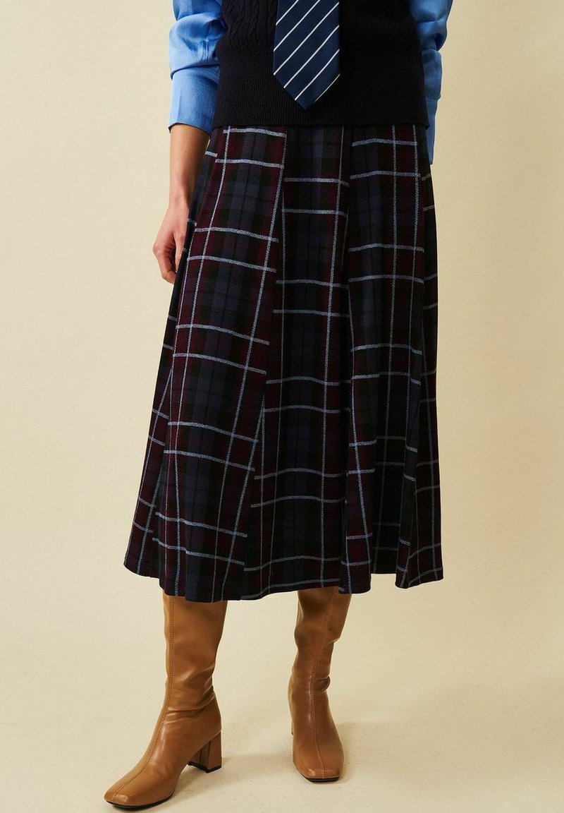 Rutigt midi-kjol i mörk burgunder, blå och svarta toner. Tyget är strukturerat, med veck och en flödande design. Återfinns i kombination med beige knähöga stövlar.