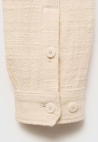 Cotton button-up shirt sleeve in soft beige, featuring textured fabric with a checkered pattern and two round, light-colored buttons.