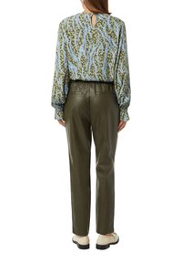 Bluse mit grünem Blumenmuster und Ballonärmeln; Ausschnitt-Detail im Rücken. Olivgrüne Lederhose mit zwei Gesäßtaschen, eng geschnitten. Cremefarbene Schuhe.