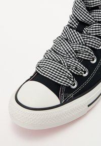 Shoe sneaker em tela preta com bico de borracha branca e sola texturizada. Apresenta atacadores em padrão gingham e costura em rosa contrastante.