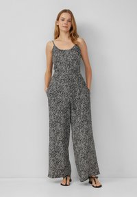 Schwarzer und weißer gemusterter Jumpsuit mit Spaghetti-Trägern, weitem Bein und seitlichen Taschen. Leichter Stoff mit geometrischem Design.