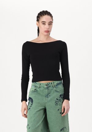 Black long-sleeve top with a boat neckline, paired with green wide-leg jeans featuring blue tie-dye patterns. Fabric appears soft and fitted.