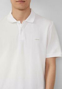 Witte polo met een klassieke kraag, gemaakt van katoen, met twee knopen en een klein geborduurd logo op de linkerkant van de borst. Korte mouwen.