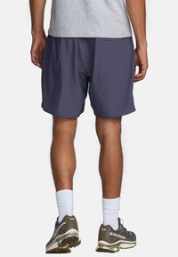 Shorts de sport pour hommes, gris foncé, à coupe ample, avec une taille élastique et un tissu lisse ; portés avec des chaussures de course grises et des chaussettes blanches.