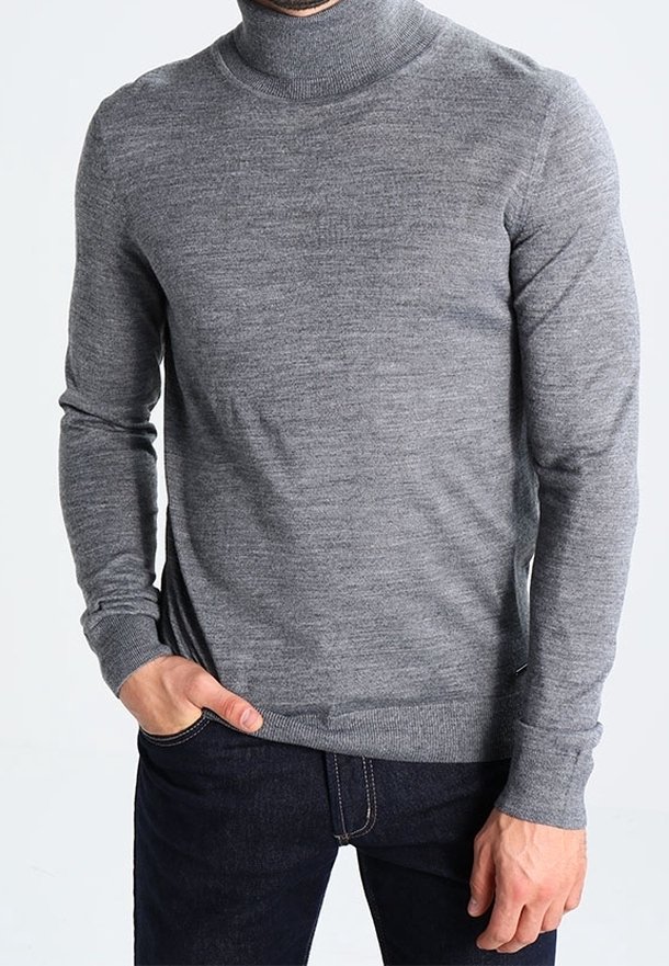 Maglione grigio a collo alto realizzato in morbido tessuto a maglia, con maniche lunghe, polsini a costine e una vestibilità aderente. Indossato con jeans scuri.
