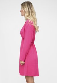 Vaaleanpunainen pitkähiha mekko, jossa rento istuvuus ja vyötärön kiristys. Mekko on valmistettu pehmeästä kankaasta, siinä on suora helma ja sileä pinta.