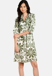 Abito con stampa floreale bianca e motivi verdi, dotato di colletto a camicia, maniche a tre quarti e cintura sul punto vita legata. Tessuto morbido e liscio.