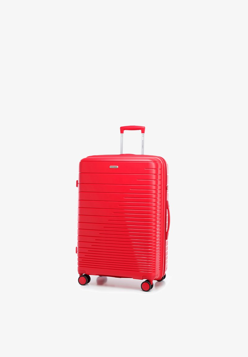 Maleta rígida roja con ranuras horizontales, asa extensible, asa lateral y cuatro ruedas giratorias sobre fondo blanco.