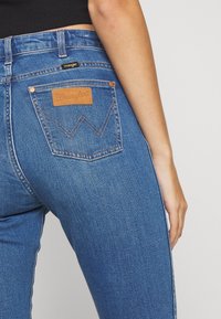 Blå denimjeans med hög midja, prydda med en läderpatch från Wrangler, kontrasterande sömmar och en figurnära design med bakfickor.