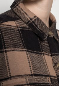 Brun och svart rutigt skjorta med klassisk krage, prydd med guldknappar och en mjuk textur som framhäver kontrasterande rutor.