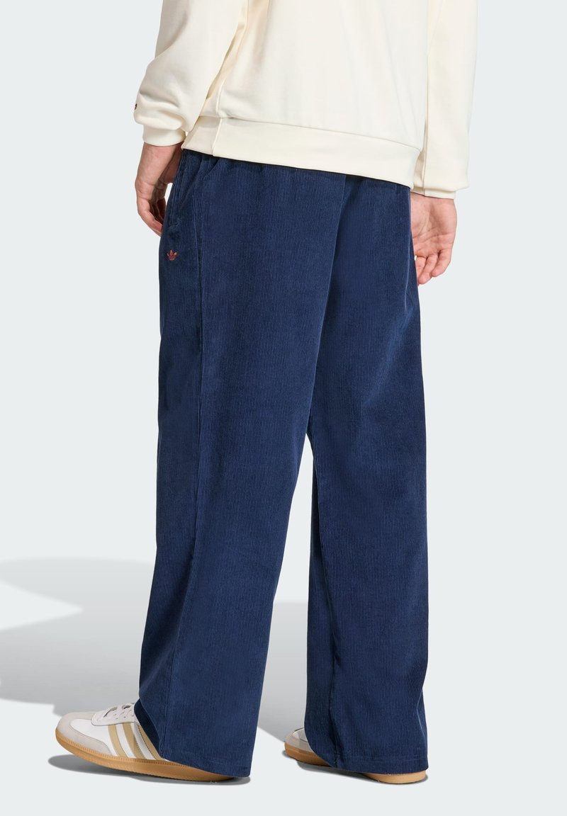 Navy corduroy wide-leg pants with side pockets. Features a subtle embroidered logo and textured fabric. Styled with white sneakers.