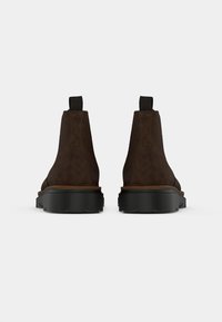 Bocanci din suede maro, la gleznă, cu vârf rotunjit, talpă din cauciuc negru și fante pentru tragere în spate. Au un design simplu și neted.