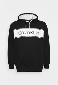 Felpa nera con accenti bianchi, caratterizzata da una tasca frontale e cappuccio regolabile con stringhe. Logo "Calvin Klein" esposto in modo prominente su una banda bianca.