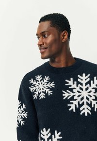 Maglione blu navy realizzato in tessuto lavorato a maglia, caratterizzato da grandi motivi di fiocchi di neve bianchi sulla parte anteriore, con scollatura rotonda e polsini a coste.