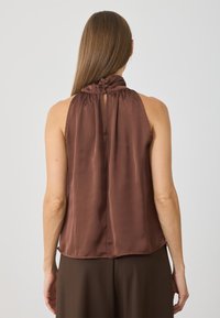Satinový hnědý halter top se skládáním na krku a otvor v zadní části. Hladká textura, uvolněný střih a zaoblený lem.