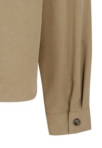 Manche de chemise beige avec un poignet maintenu par un seul bouton foncé, montrant une fine texture de tissu tissé et des détails de couture.