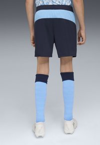 Jūras spēku sporta šorti ar gaiši zilu jostas paneli. Gaiši zila ceļgala augstuma zeķes ar teksturētu rakstu. Baltas futbola zābaki ar gaiši pelēkiem akcentiem.