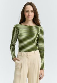 Groen en wit gestreepte lange mouw top met een bootnek, gecombineerd met beige op maat gemaakte broeken. Gladde stof, aansluitend ontwerp.