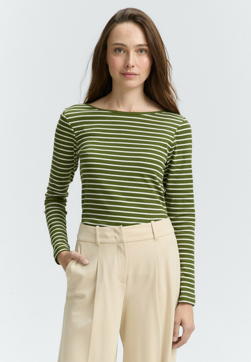 Haut à manches longues rayé vert et blanc avec un décolleté bateau, associé à un pantalon beige ajusté. Tissu lisse, design près du corps.