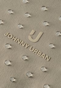 Stoff mit geprägtem Tupfenmuster und erhabenem Schriftzug "JOHNNY URBAN" neben einem stilisierten "J"-Logo.