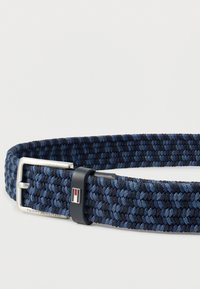 Blue and black braided fabric belt with silver metal buckle and black leather loop featuring red, white, and blue rectangular emblem.