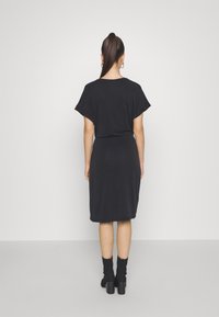 Schwarzes Midi-Kleid mit kurzen Fledermausärmeln, tailliertem Schnitt und weicher Textur. Getragen mit knöchellangen schwarzen Socken und Schuhen mit dicken Absätzen.
