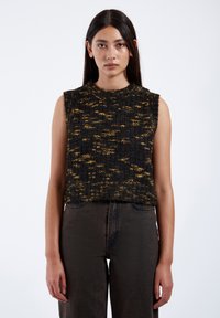 Stickad ärmlös topp i svart och gult med en strukturerad mönster. Har en rund halsringning och en avslappnad passform. Matchad med mörka denimjeans.