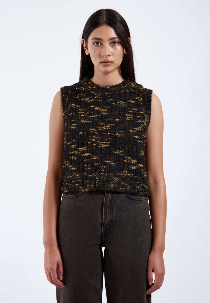 Stickad ärmlös topp i svart och gult med en strukturerad mönster. Har en rund halsringning och en avslappnad passform. Matchad med mörka denimjeans.