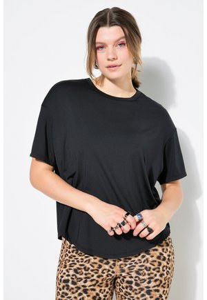 Zwarte T-shirt met korte mouwen in een relaxte fit, gecombineerd met een patroon van panterprintbroeken. Het model draagt meerdere ringen.