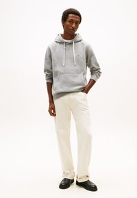 Szürke kapucnis pulóver fehér zsinórokkal, kenguruzsebbel, krémszínű nadrággal és fekete, könnyen felvehető cipőkkel párosítva. Egyszerű, kényelmes fazon.