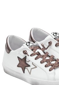 Baskets en cuir blanc avec des accents métalliques bruns, un patch en forme d'étoile brun, des lacets à imprimé léopard et un design à profil bas.