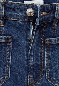 Jeans iz jeansa v temno modri barvi, s vidnim oranžnim šivanjem, kovinskim gumbom za zapiranje in zadrgo spredaj.