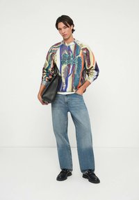 Multicolored sweatshirt with graphic text, light blue wide-leg jeans, and black leather shoes. Black tote bag in hand.