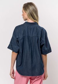 Donkerblauw denim overhemd met korte mouwen, een omgeslagen kraag en een licht gebogen zoom, met een plooidetail op de achterkant.