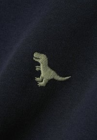 Tela marina con un pequeño diseño de dinosaurio bordado en verde texturizado, que muestra una costura suave y una textura blanda.