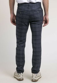 Pantalon à motif écossais marine avec une coupe slim, doté de deux poches arrière avec des boutons et d'une texture lisse. Porté avec des baskets claires.